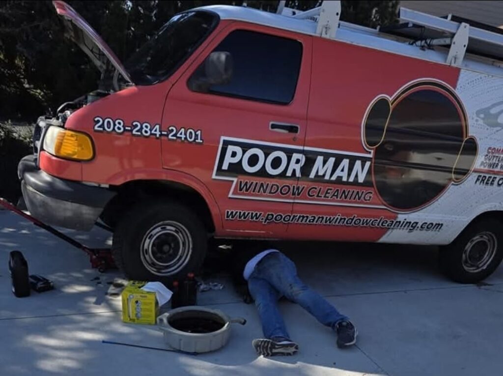 Reid Pinther working underneath the Poor Man Window Cleaning van in a driveway