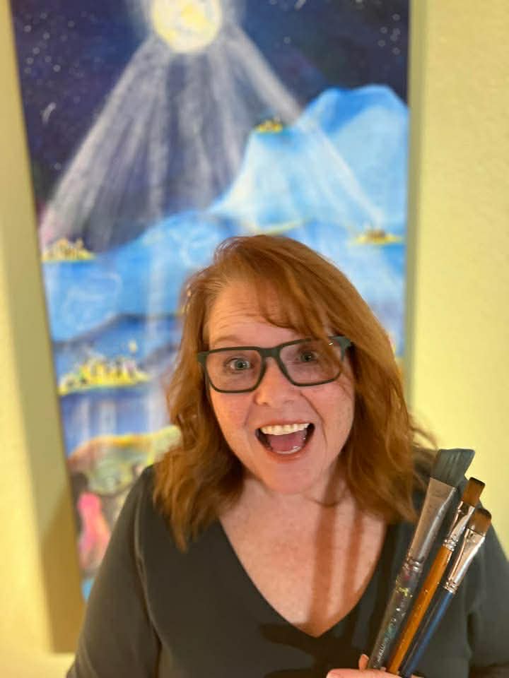 Karen Gillette laughing and holding paintbrushes in front of one of her vibrant blue paintings